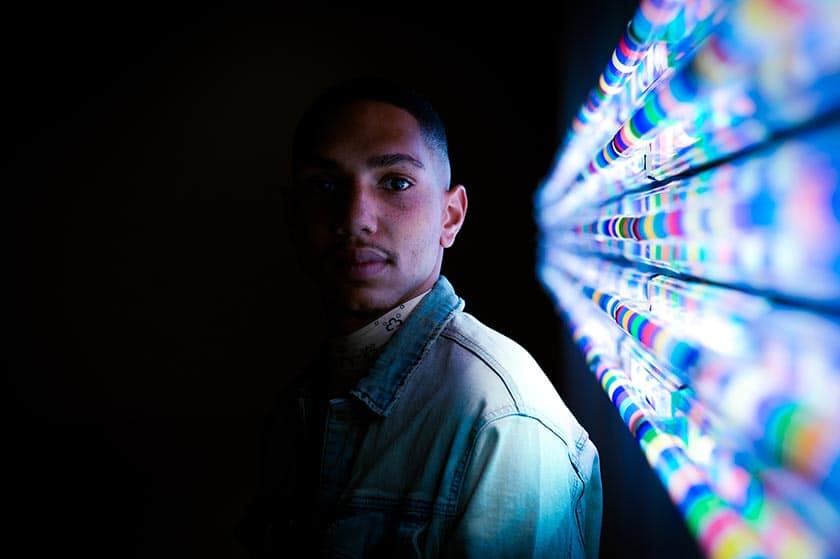 portrait of a black man lit on one side by bars of colorful striped lights