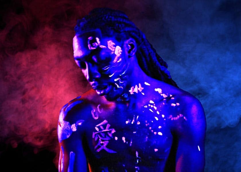 portrait of black man in mixed blue and red light, with glowing designs painted on his skin