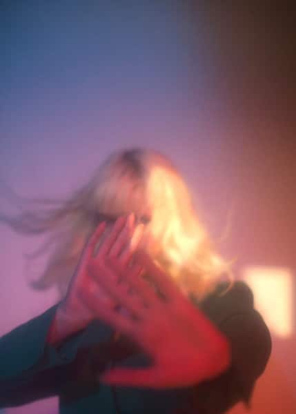 figure in soft focus with blond hair, their hands obscuring their face
