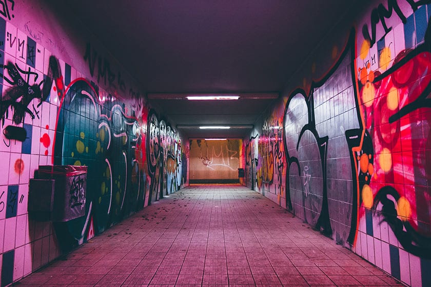 a subway hall covered in colorful graffiti and lit with fluorescent overhead lights