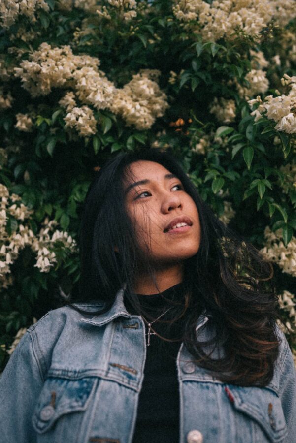 teen girl standing near white petaled flowers wearing a denim jacket