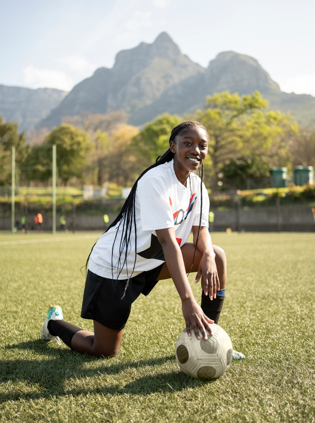 female black teen soccer player with long braids posing with a soccer ball on the field