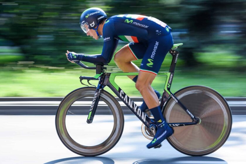 man wearing blue cycling gear and helmet riding a road bicycle at high speeds