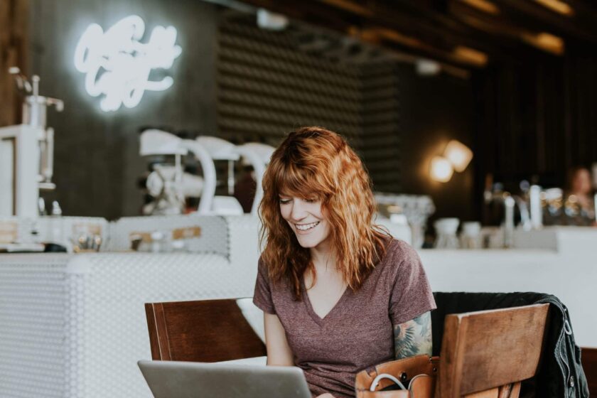 woman with red hair sitting with laptop in a cafe