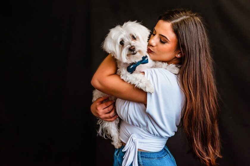 Studio Pet Mini Session with fluffy white haired dog being held by a woman with long brown hair and a blue shirt. Portrait by Jani Tzolov of JS Portrait Studios