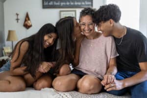 Portrait of happy mother holding hands and sitting with her three teen children. Photo by Jared Lazarus.