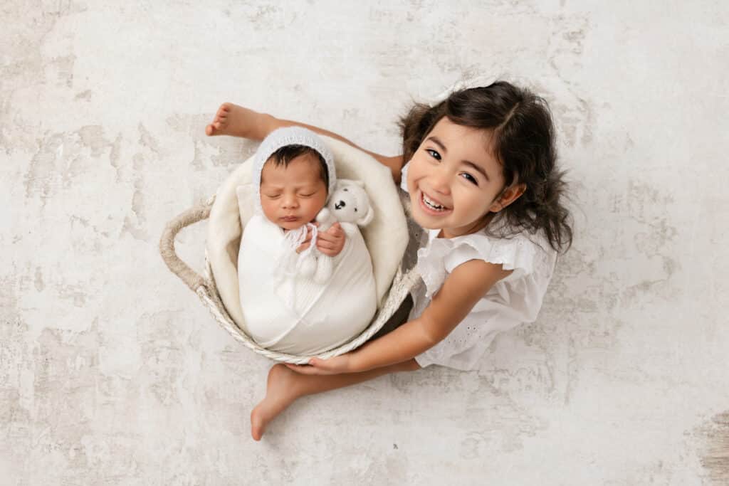 Image by Stephanie Schnautz: a baby posed in basket by sibling