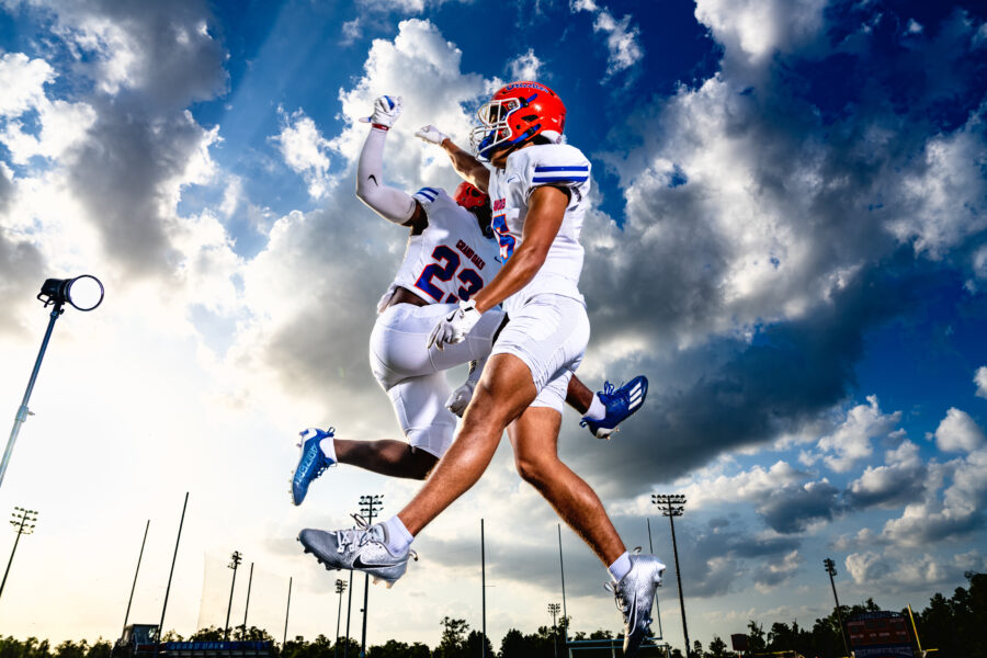 two highschool football players jumping in the air and doing a high five