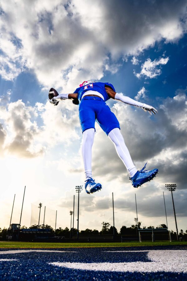 football player with blue and white uniform leaping in air holding a football