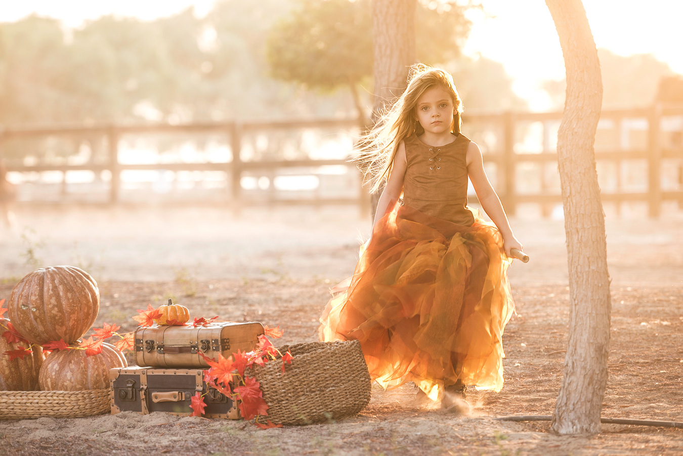 Girl in autumnal dress, holding stick, near pumpkins and vintage suitcases