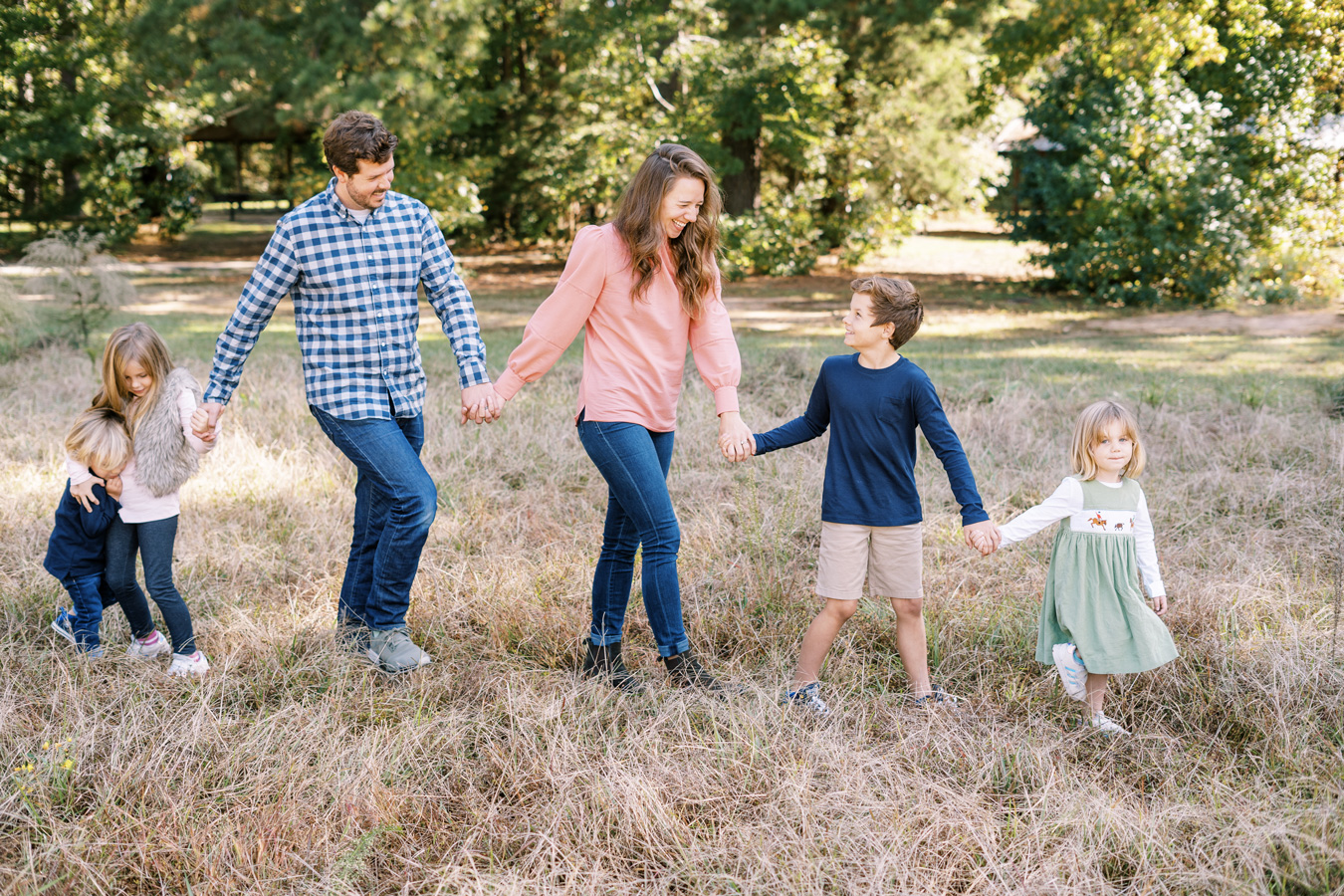 Family of five holding hands, walking in a grassy field