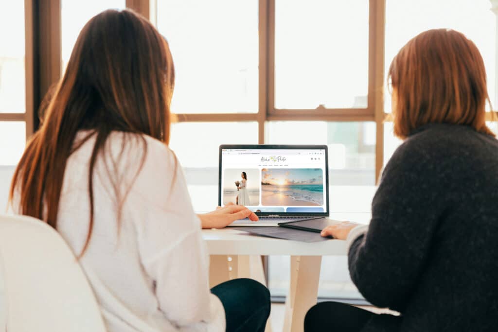 Two women sitting beside each other looking at website on laptop