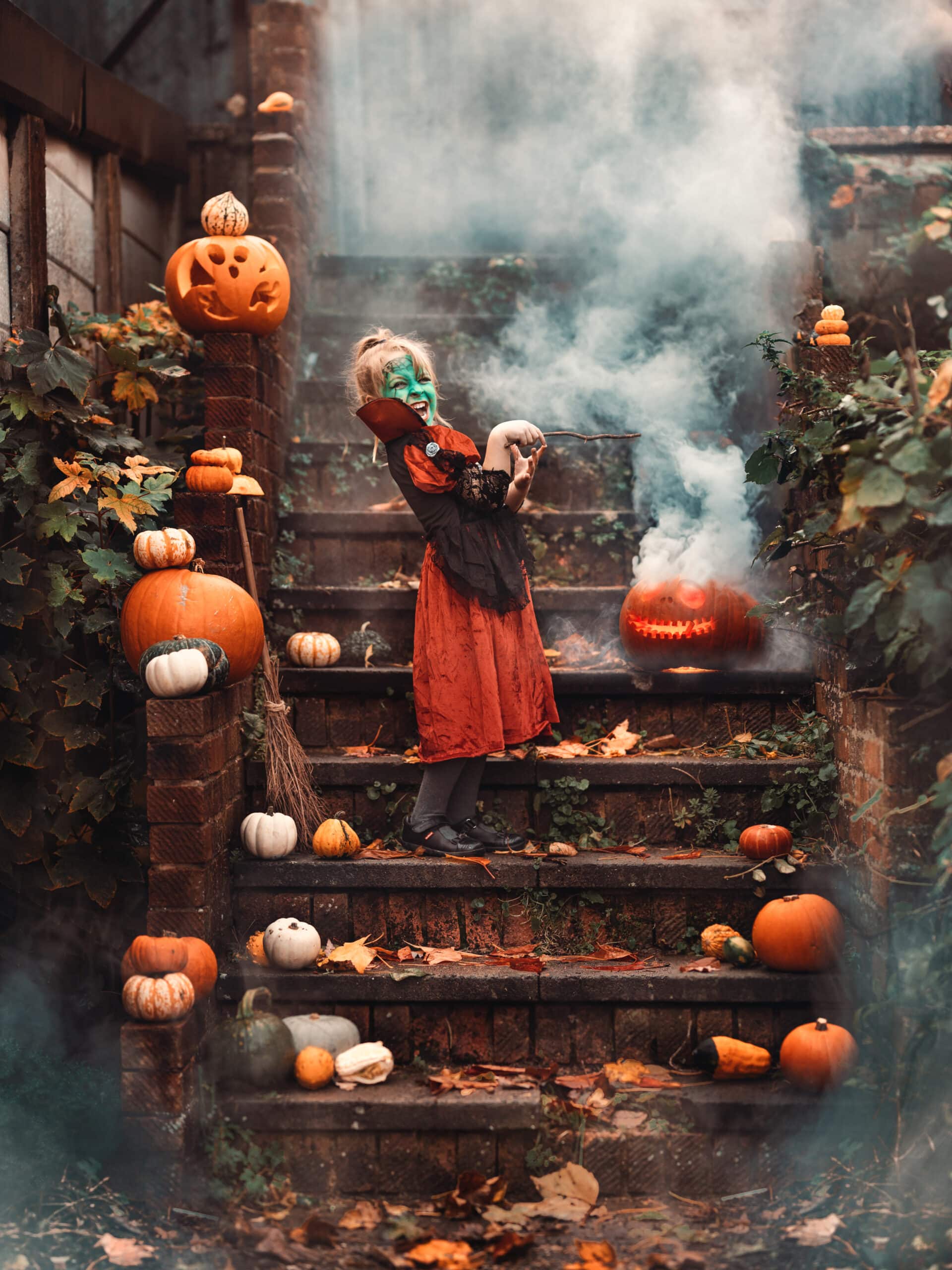 girl wearing witch costume and holding wand surrounded with collection of pumpkins