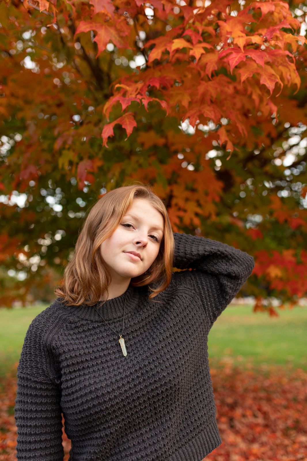 teen girl in grey sweater posing near autumn foliage