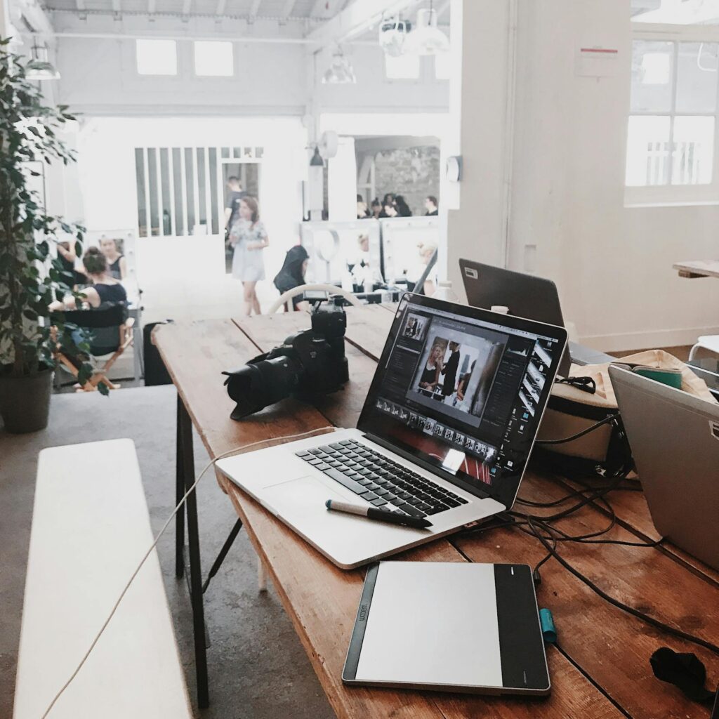 A bright, modern photography workspace featuring laptops, a camera, and a drawing tablet