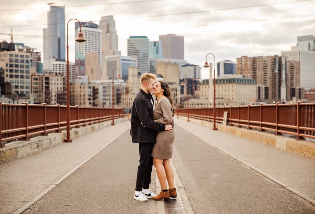 Photo by GraceLyn Lee of a couple on a bridge with a cityscape behind them and almost kissing