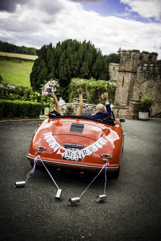 wedding couple riding away from reception in red classic topless car with "just married" bunting. photo by Duncan Edward