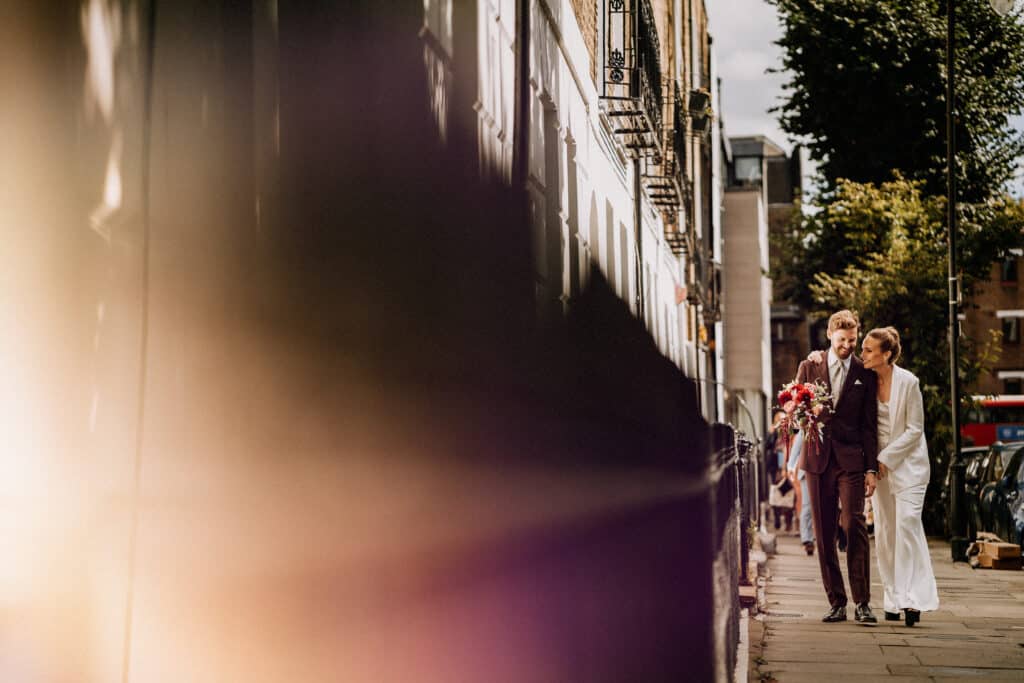 wedding couple laughing and walking close together alongside a building. Photo by Steve Bridgwood