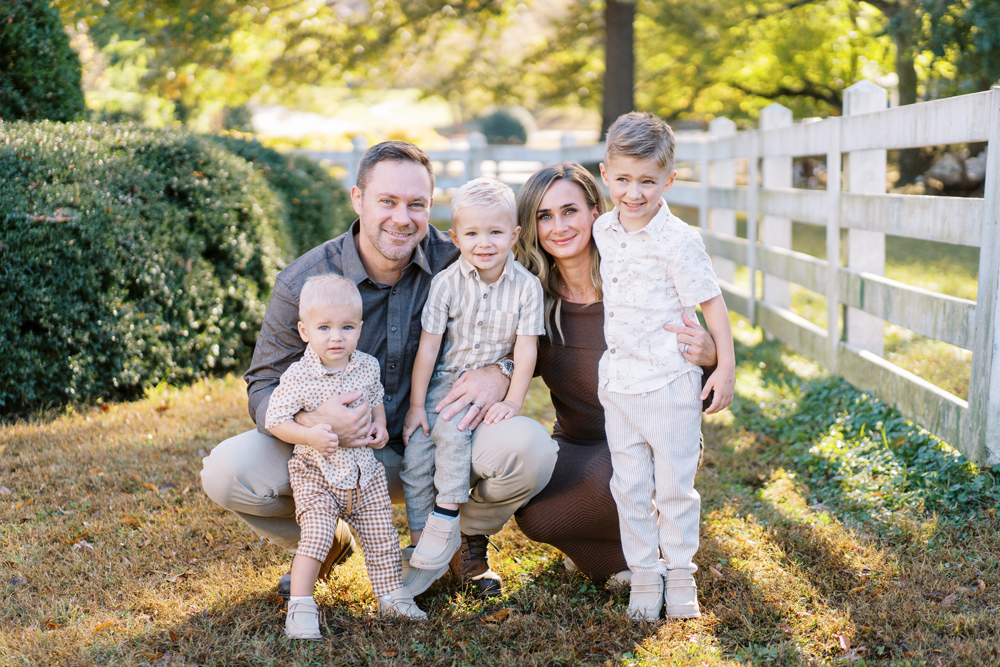 Family portrait: parents and three young sons smiling, outdoors near a white fence