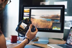 personholding camera while editing landscape photograph on their desktop computer