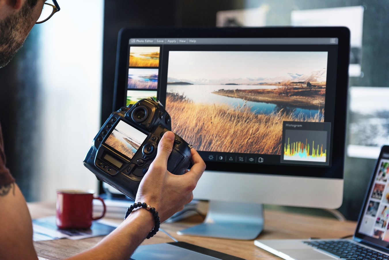 personholding camera while editing landscape photograph on their desktop computer