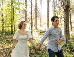 portrait of a man and woman holding hands while he leads her through the woods by Heather Nelson.