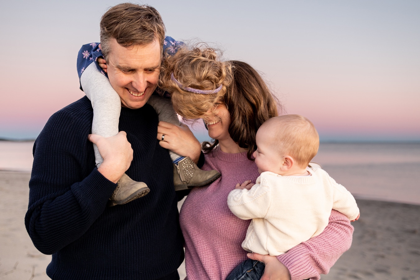 portrait of mom holding baby and toddler girl sitting on dads shoulders on the beach at sunset by Wild Orchard Studios Photography