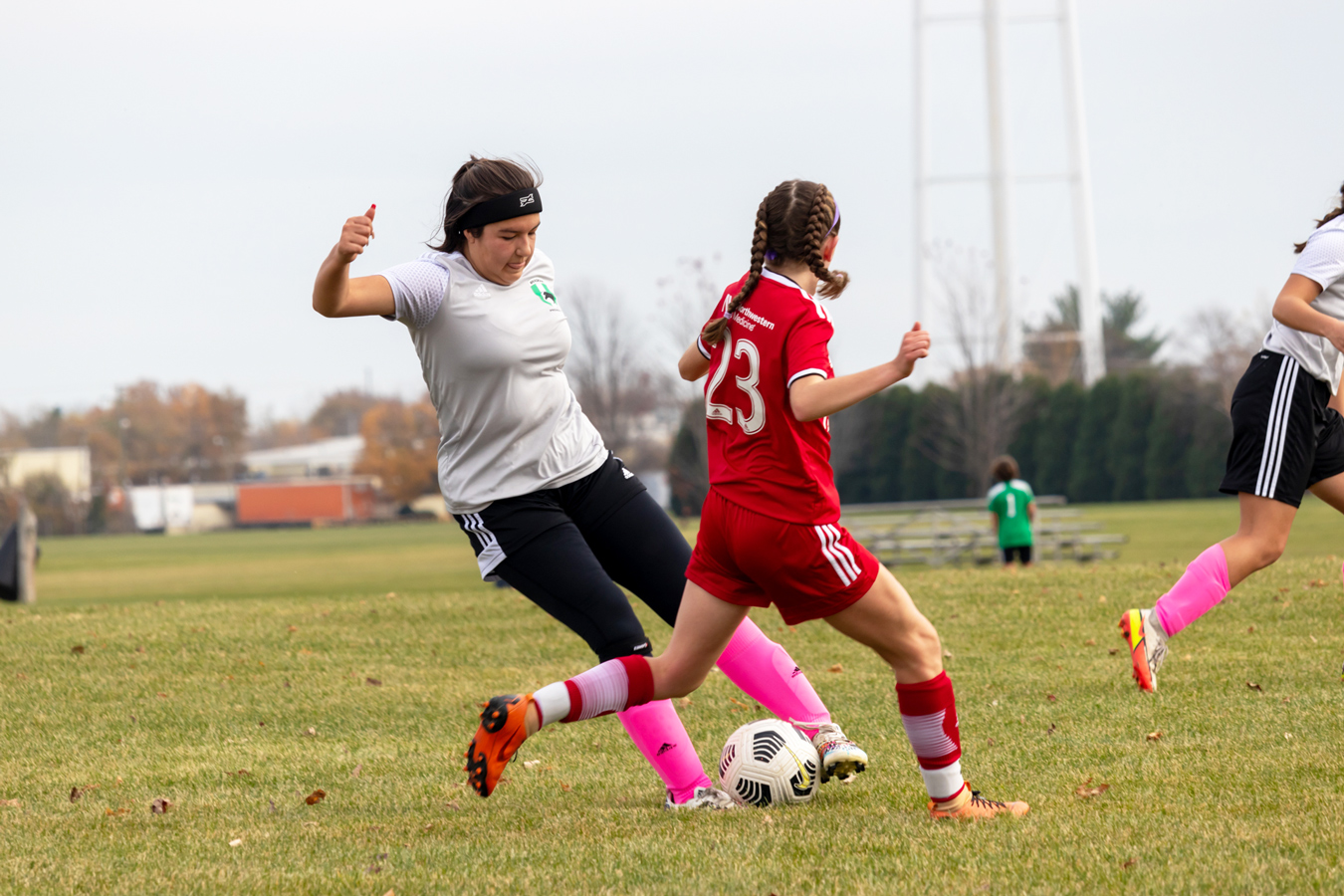 Two female soccer players vying for the ball; one in a red jersey, the other in gray
