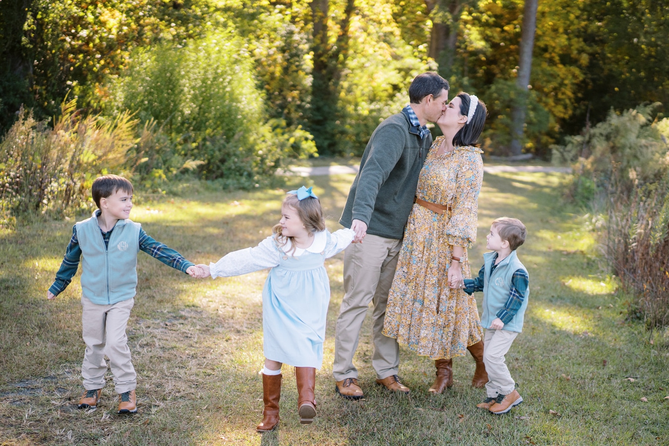 Mom and dad kissing while holding hands with their daughter and two sons in a grassy path Strombom Elizabeth Tate Photography