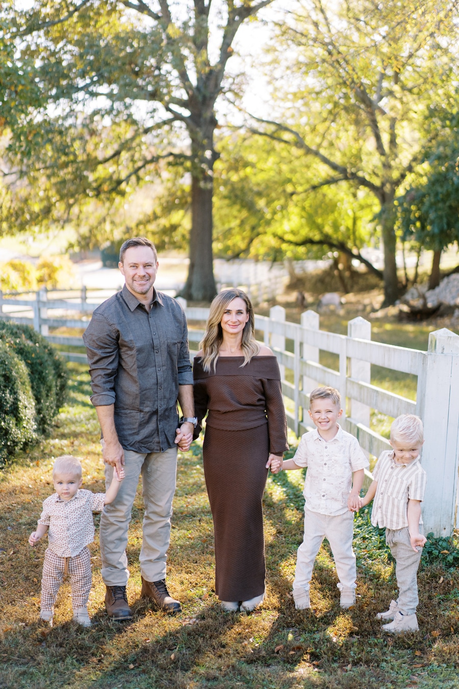 Mom dad and three little boys holding hands beside a white fence Hensberger Elizabeth Tate Photography