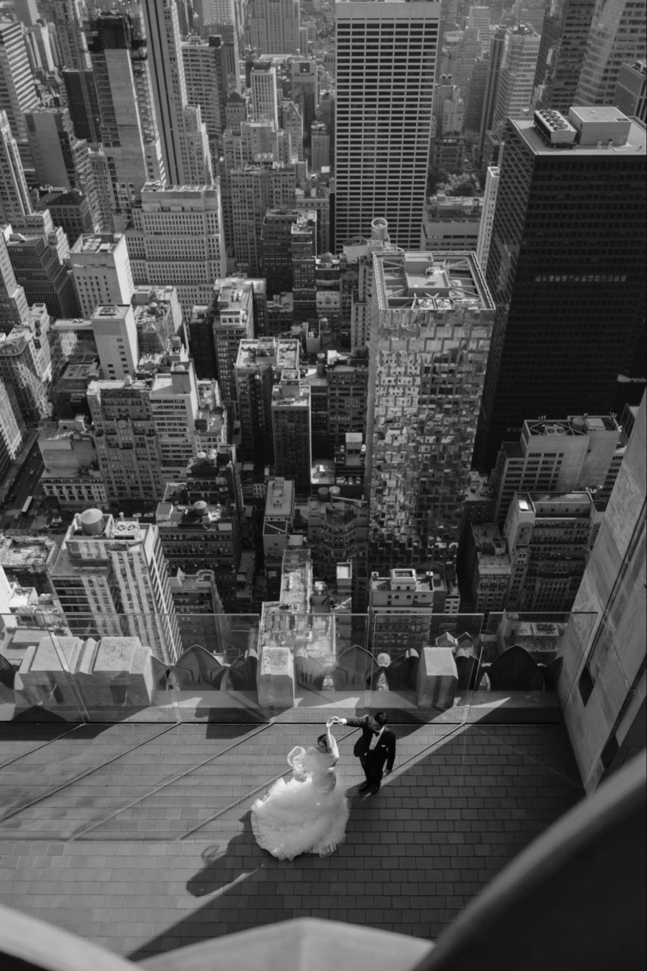Black and white photo: a bride and groom dance on a rooftop overlooking a cityscape. Photo by Renata Zimmer.