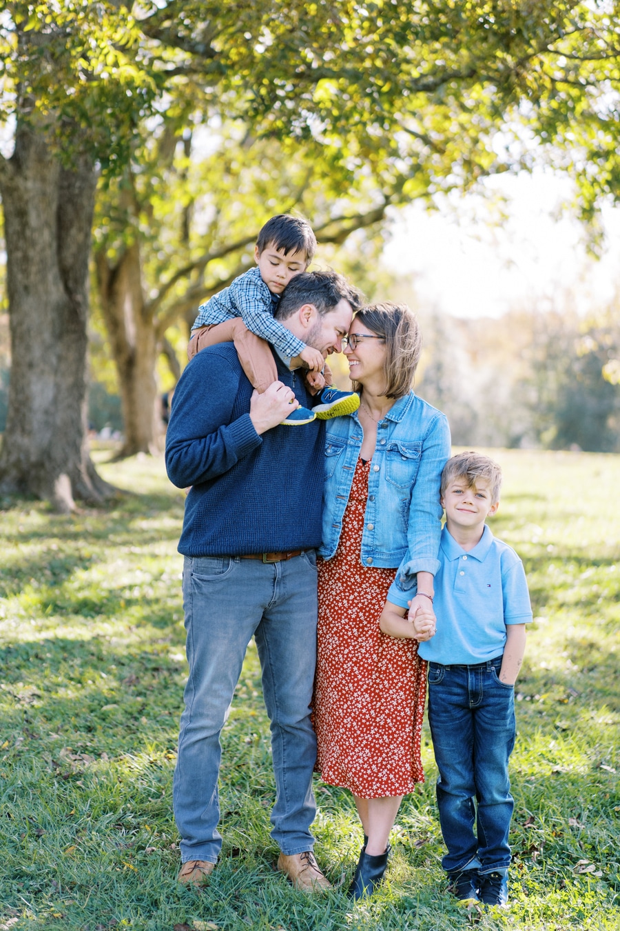 mom and dad standing close with foreheads touching while mom holds little boys hand and second little boy sits on dads shoulders Paschal Elizabeth Tate Photography