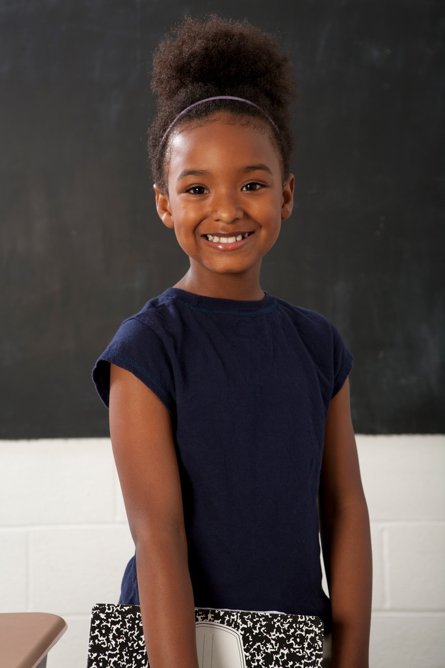 school portrait of young black girl with a curly ponytail holding a notebook