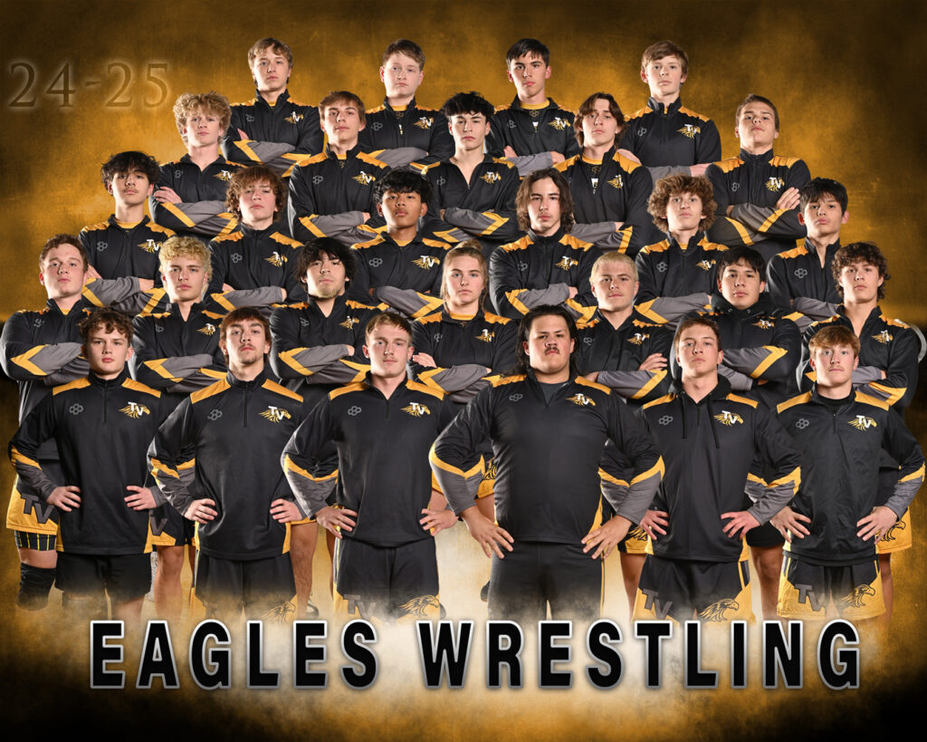 A team photo of the "Eagles Wrestling" team, consisting of approximately 30 young men, posed in rows against a gold and black background. They are wearing matching black and gold athletic jackets and shorts, with the team logo visible on their apparel.