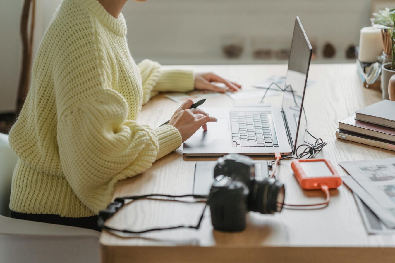 Cropped image of a female photographer using laptop while sitting at table with camera and hard drive after uploading images.