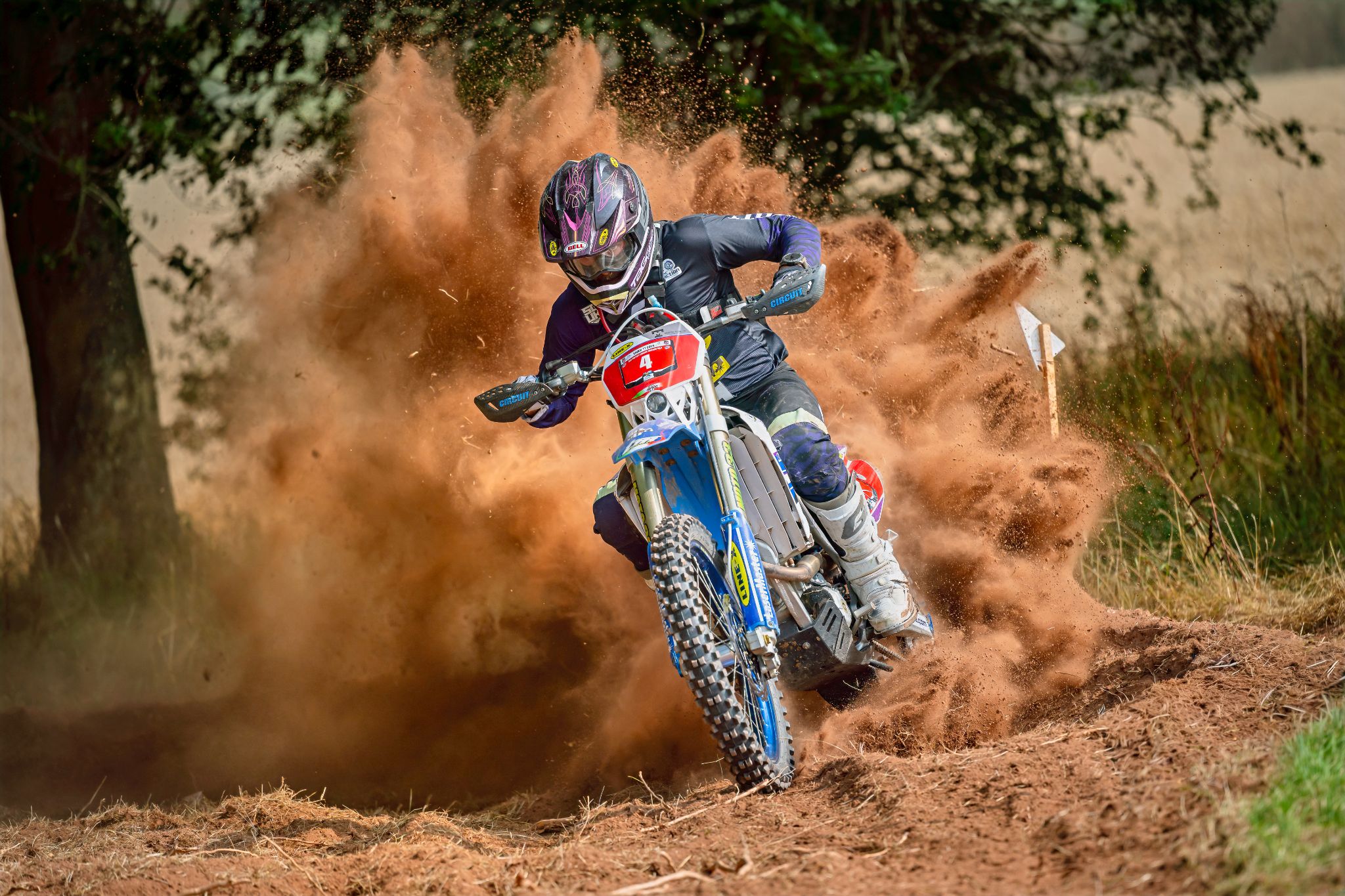 Motocross rider leaning into a dirt trail turn with dust flying