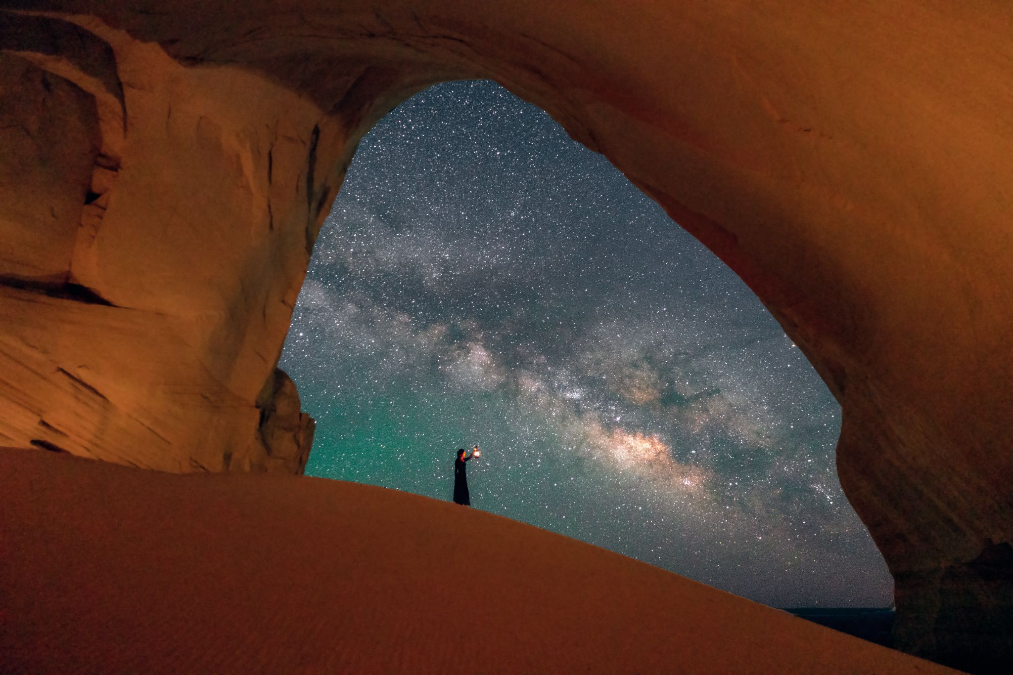 Milky Way galaxy framed by a Utah sandstone arch with silhouetted photographer