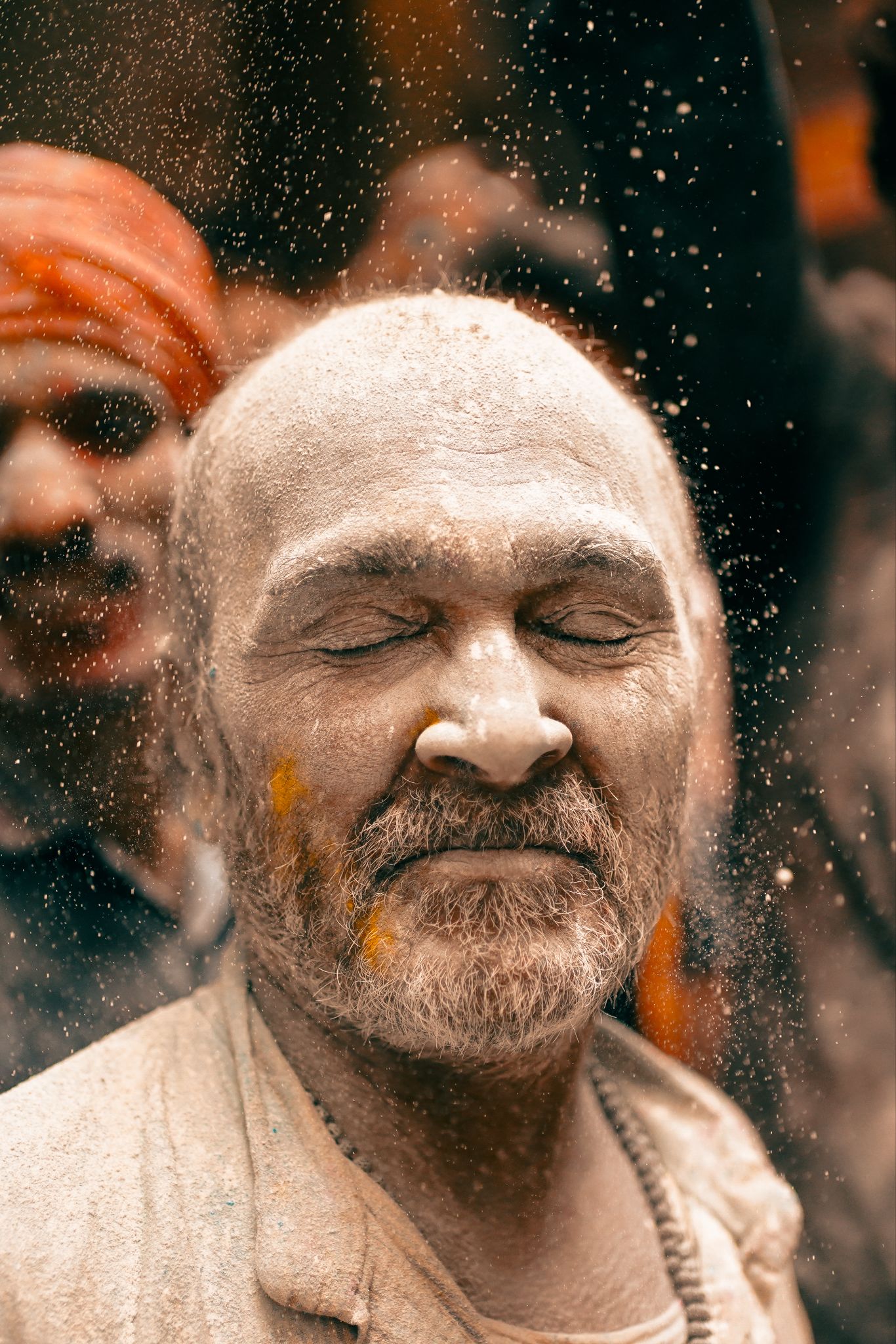 Man with closed eyes covered in colorful Holi powder during a Kashi street celebration